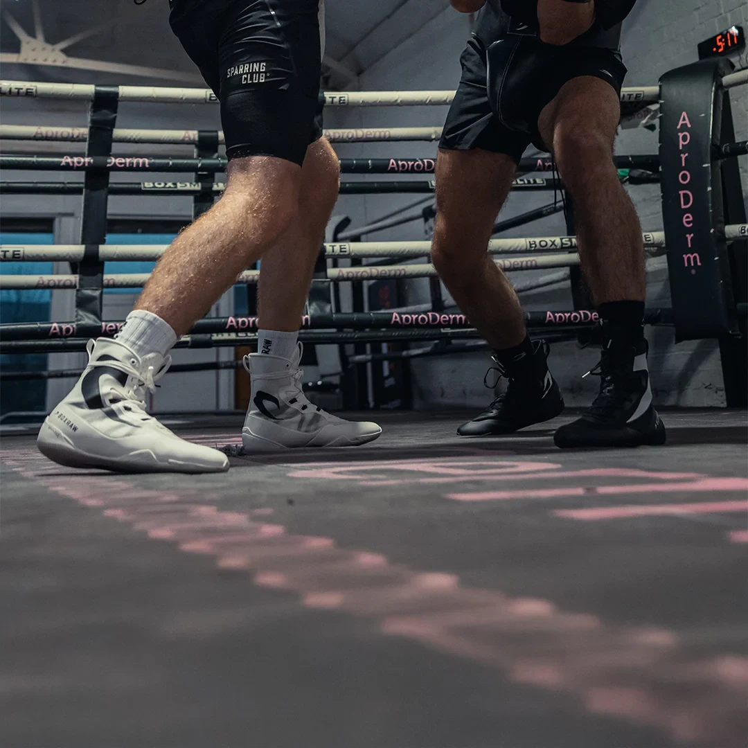 Boxing shoes and legs stepping across a pink-lit ring floor