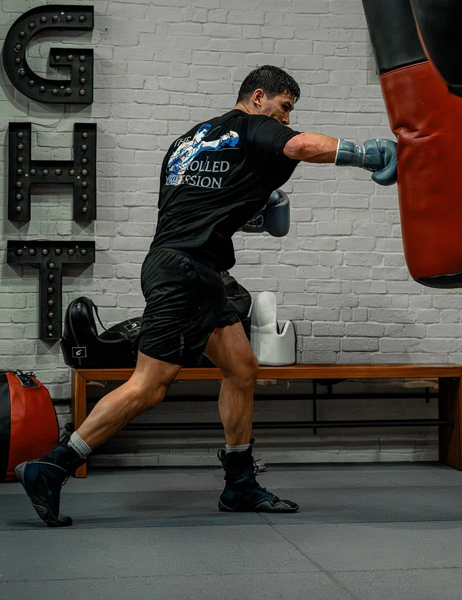 Dmitry Bivol throwing a punch at a heavy bag in a gym with a lettered wall