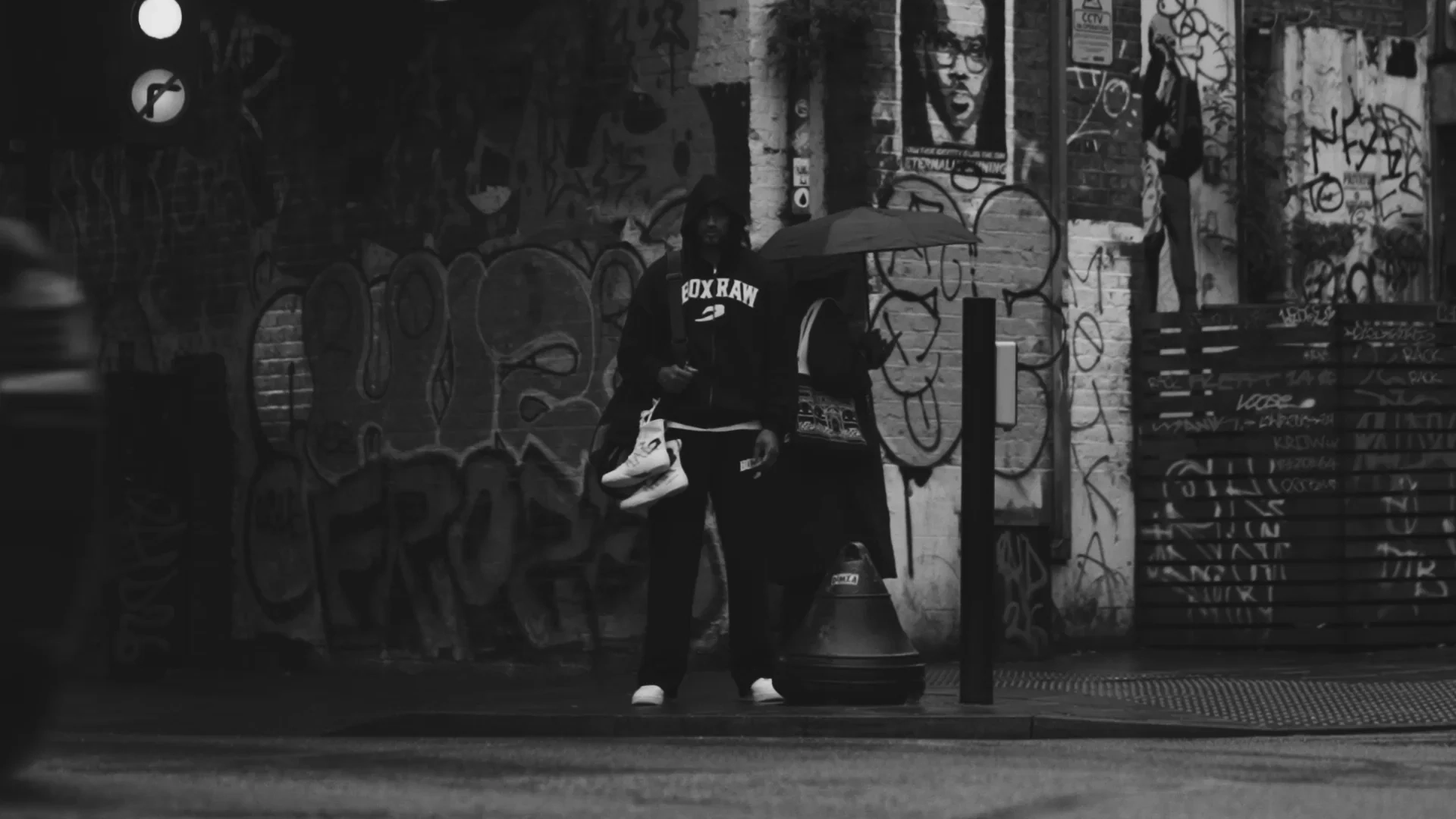 A black-and-white alley scene with hooded figures in front of a mural