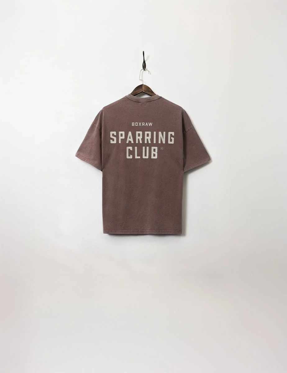 A washed brown Sparring Club T-shirt on a wooden hanger
