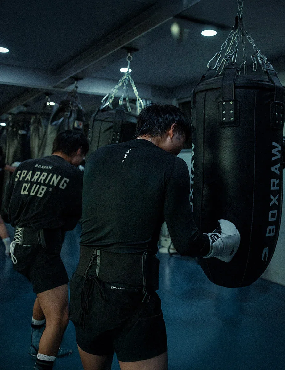 A fighter leaning into a heavy bag in a black Sparring Club top