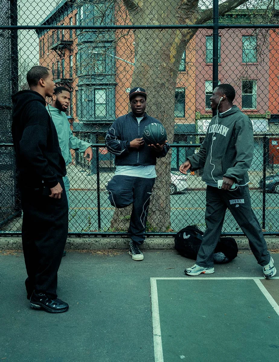 Four friends in track tops talking beside a chain-link court