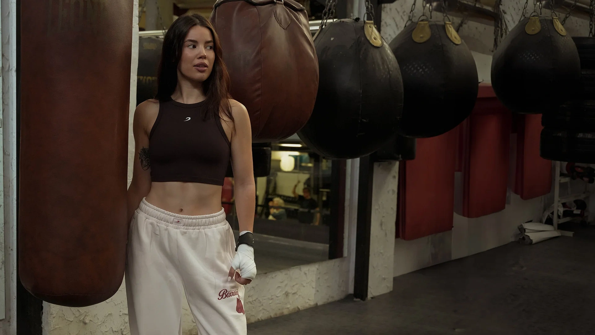 A woman in a ribbed tank top between leather punch bags