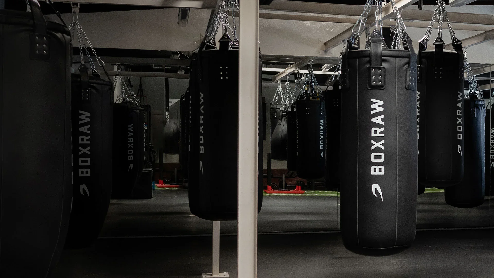 A row of tall black BOXRAW punch bags hanging in a gym