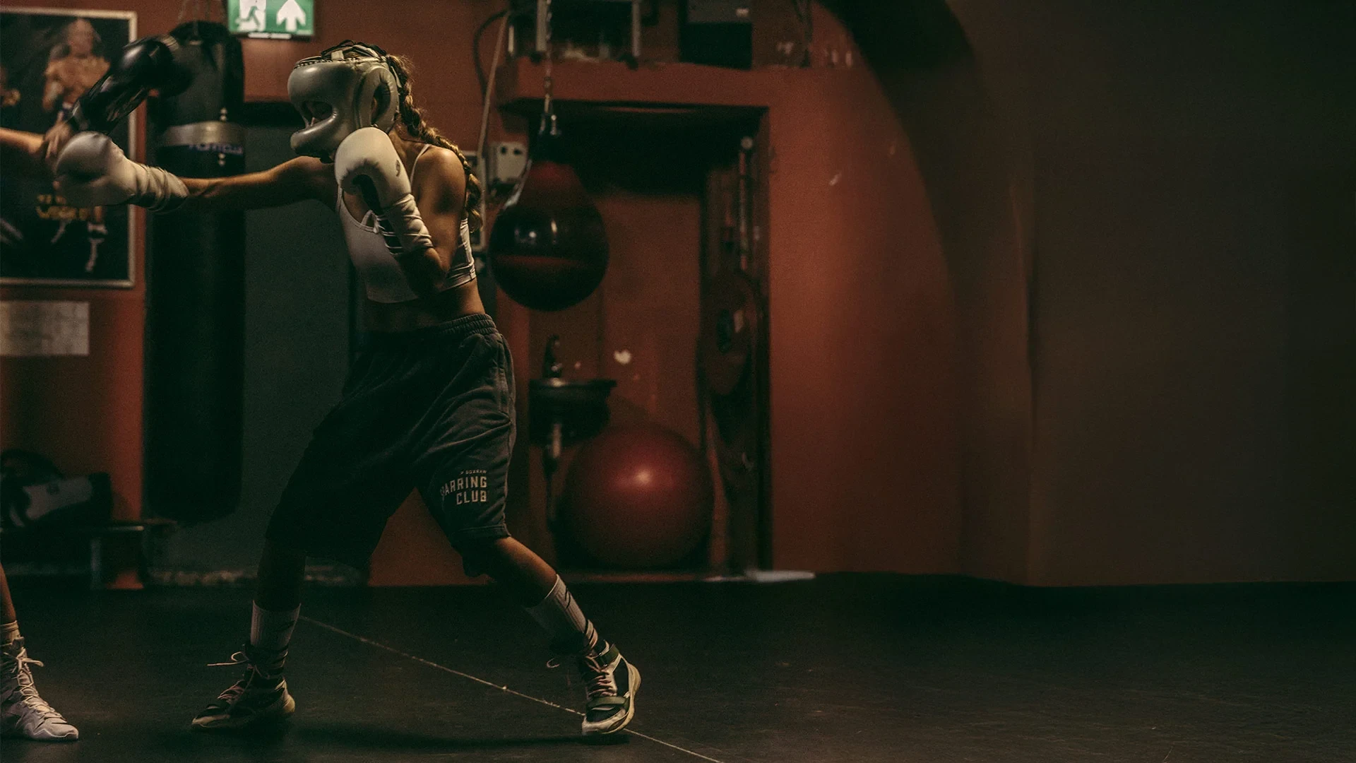 A boxer working the pads in a dim, warm-lit gym