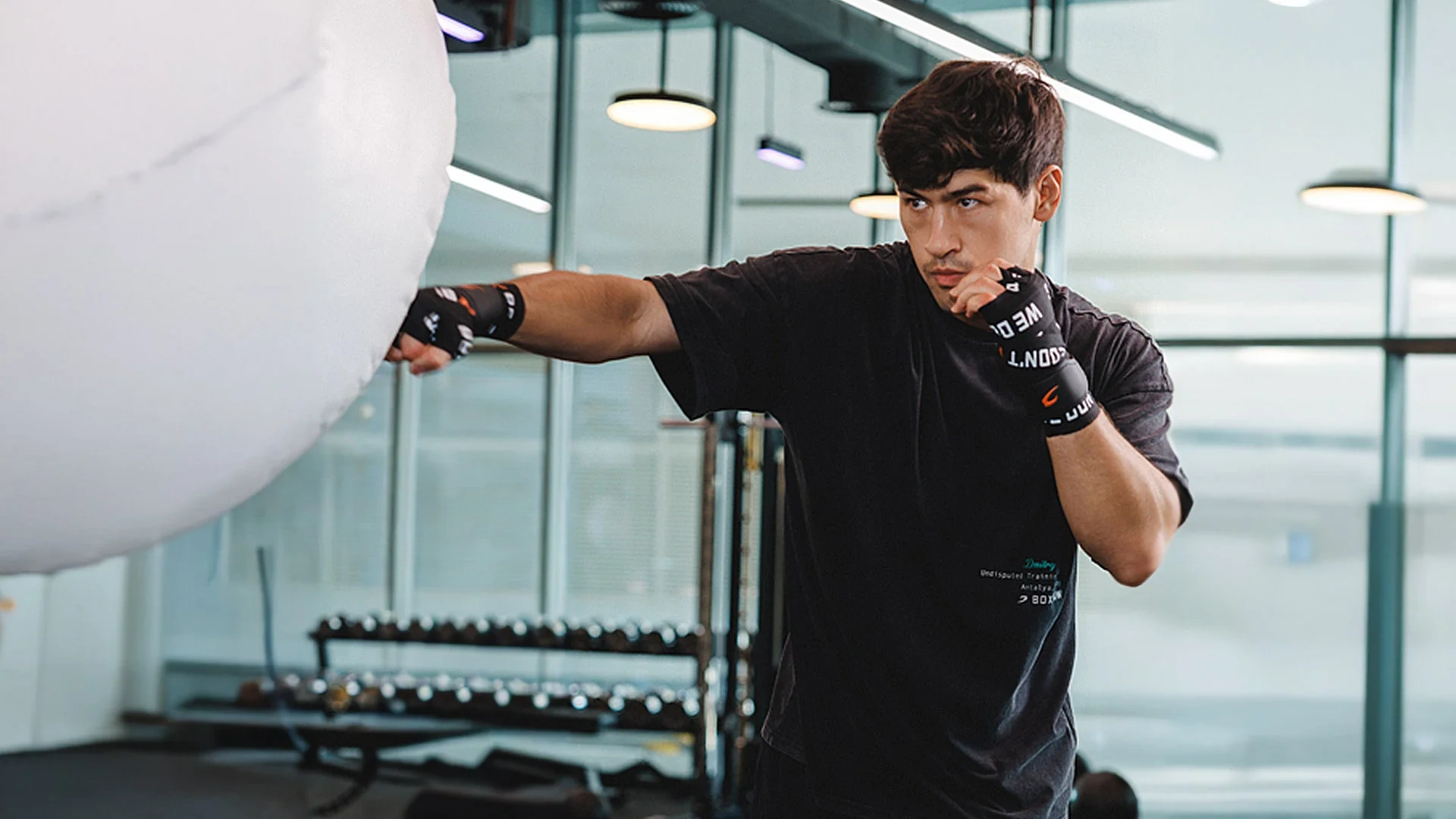 A boxer in a black top punching in a bright, white-walled gym